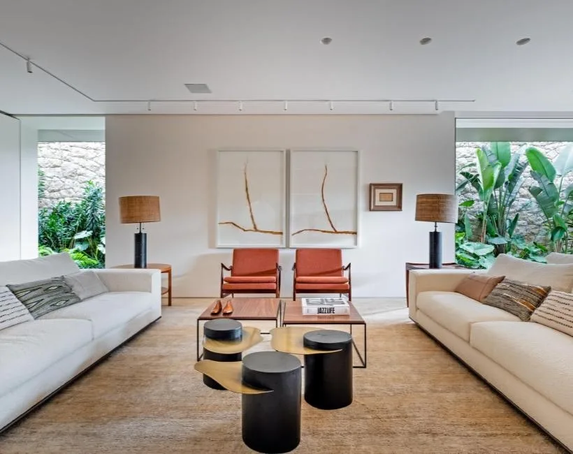 Sala de estar ampla com sofás brancos, paredes claras e muita luz natural, decorada com toques de madeira e plantas
