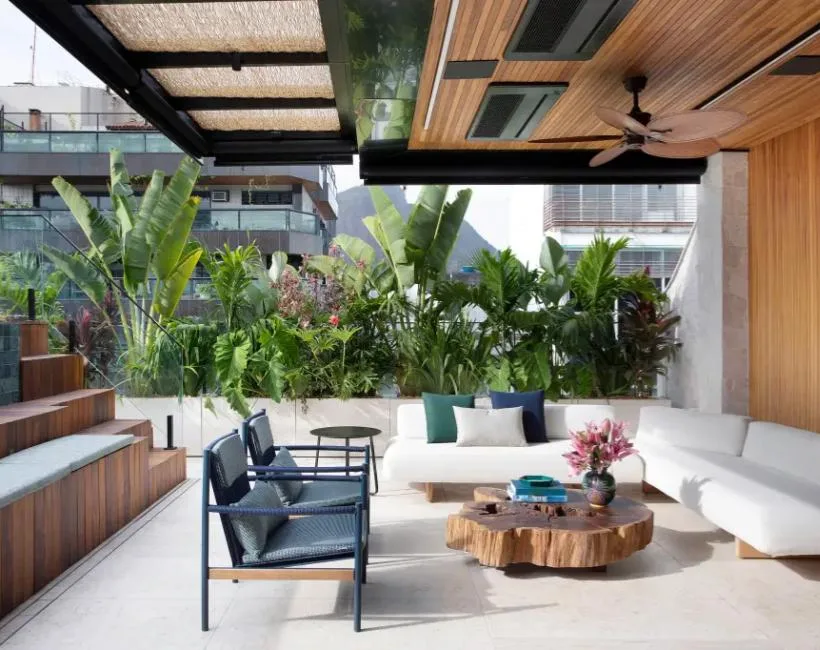Terraço moderno com teto de madeira, mobiliário branco e plantas tropicais em vaso.