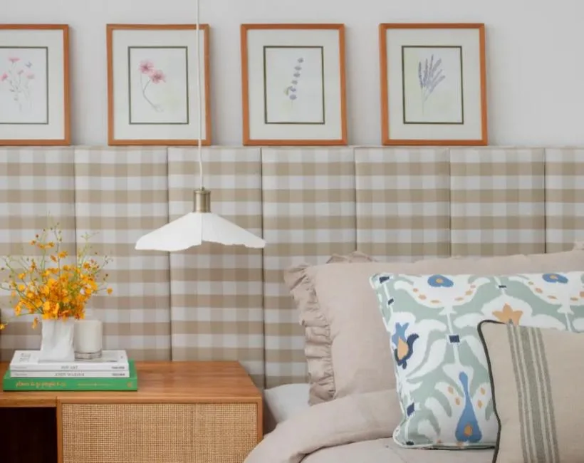 Quarto com cabeceira estofada em xadrez vichy e quadros de arte floral.