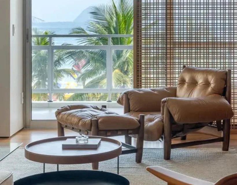 Sala de estar com painel muxarabi de madeira e poltrona de couro, com vista para o mar.